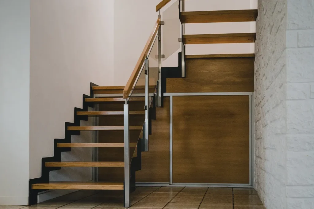 Drewniane schody wewnętrzne z metalową balustradą.