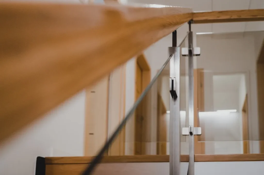 Szklana balustrada z drewnianą poręczą w nowoczesnym wnętrzu.